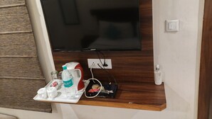 A flat-screen TV mounted on a wooden wall, a tray with a water bottle, coffee cups, and a kettle. - DREAM INN (Lucknow)