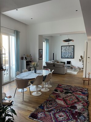 Un vaste espace de vie comprenant une table à manger, des canapés et un tapis aux couleurs vives.