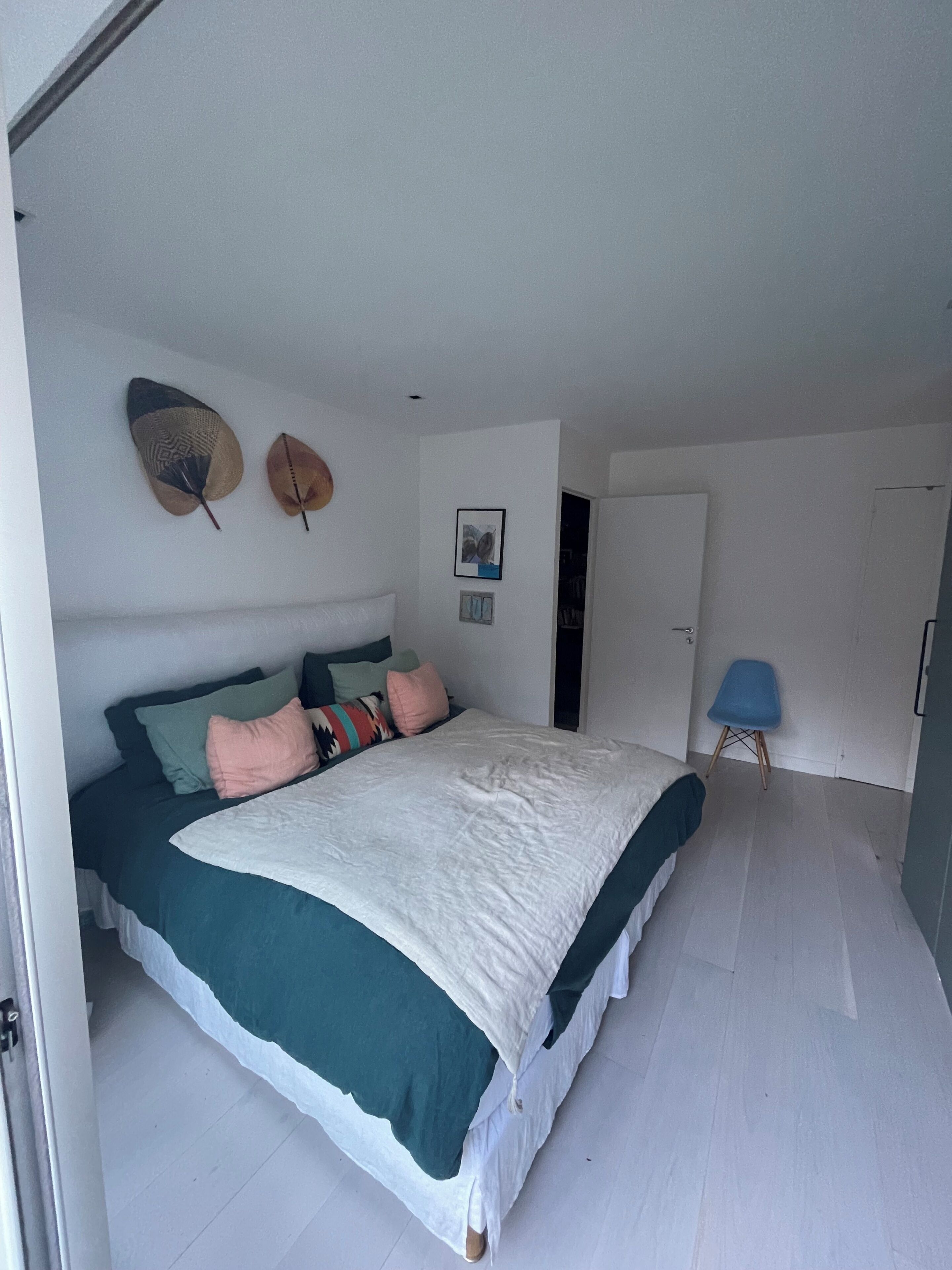 Un dormitorio con cama, almohadas, un sombrero colgado en la pared y una puerta.