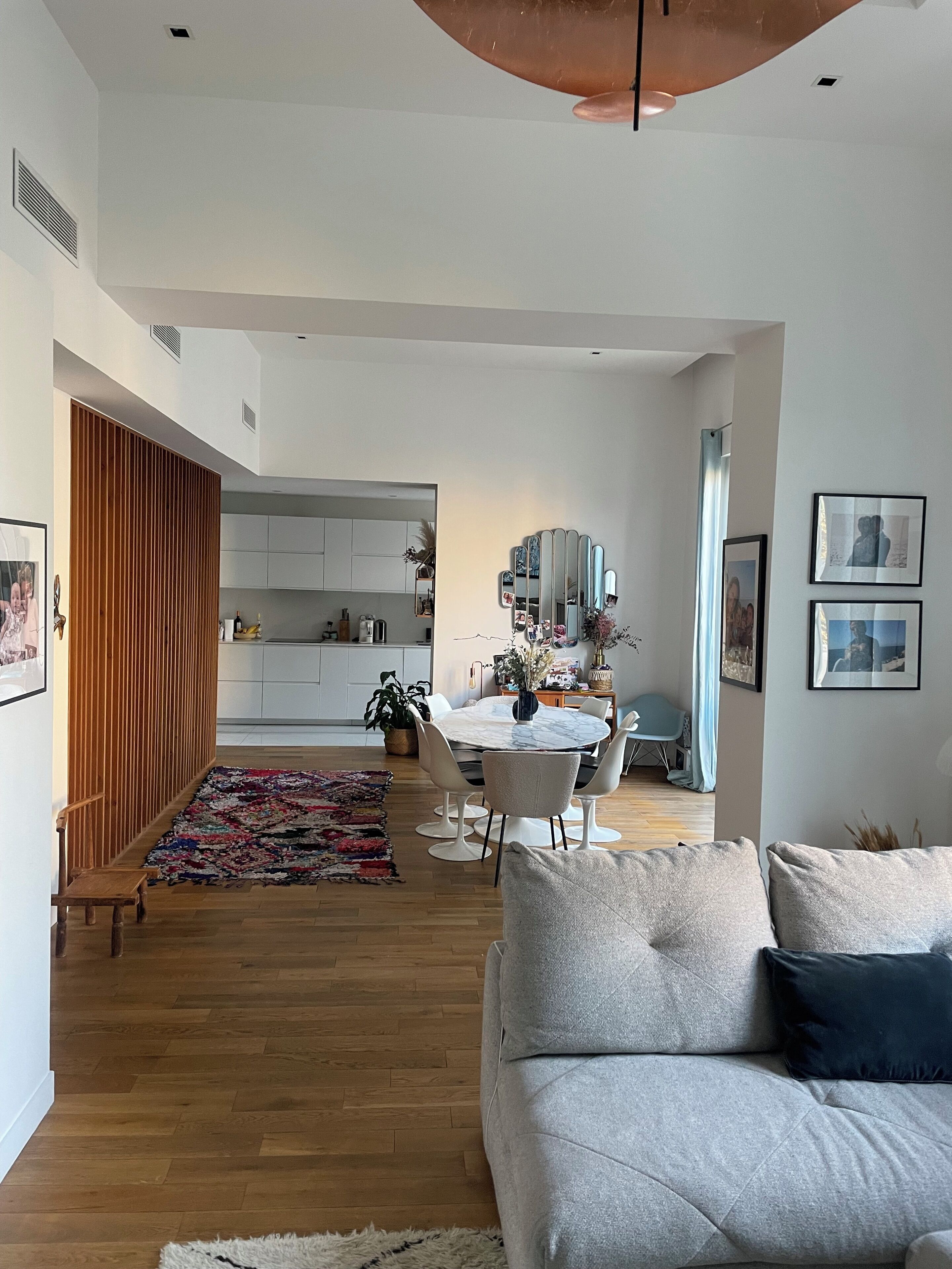 A modern living room with a sofa, a dining area with a round table, and a kitchen in the background.