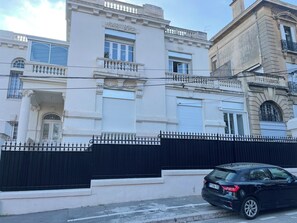 A building with a black fence, a black car parked in front, and a clear sky. - The Place to Be: Monticelli Square (Marseille)