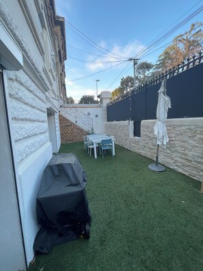 A backyard with artificial grass, a table and chairs, a barbecue grill, and a covered umbrella. - The Place to Be: Monticelli Square (Marseille)