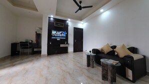 A modern living room with a flat-screen TV, a ceiling fan, a sofa, a coffee table, and a desk with a chair. - Hotel Anchor (Ranchi)