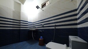A bathroom with striped tile walls, a toilet, a sink, and a shower. - Hotel Anchor (Ranchi)