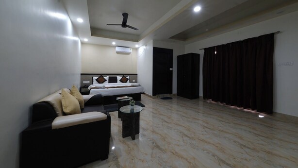 Habitación de hotel con cama, sofá, mesa de centro, ventilador de techo y un amplio ventanal con cortinas.