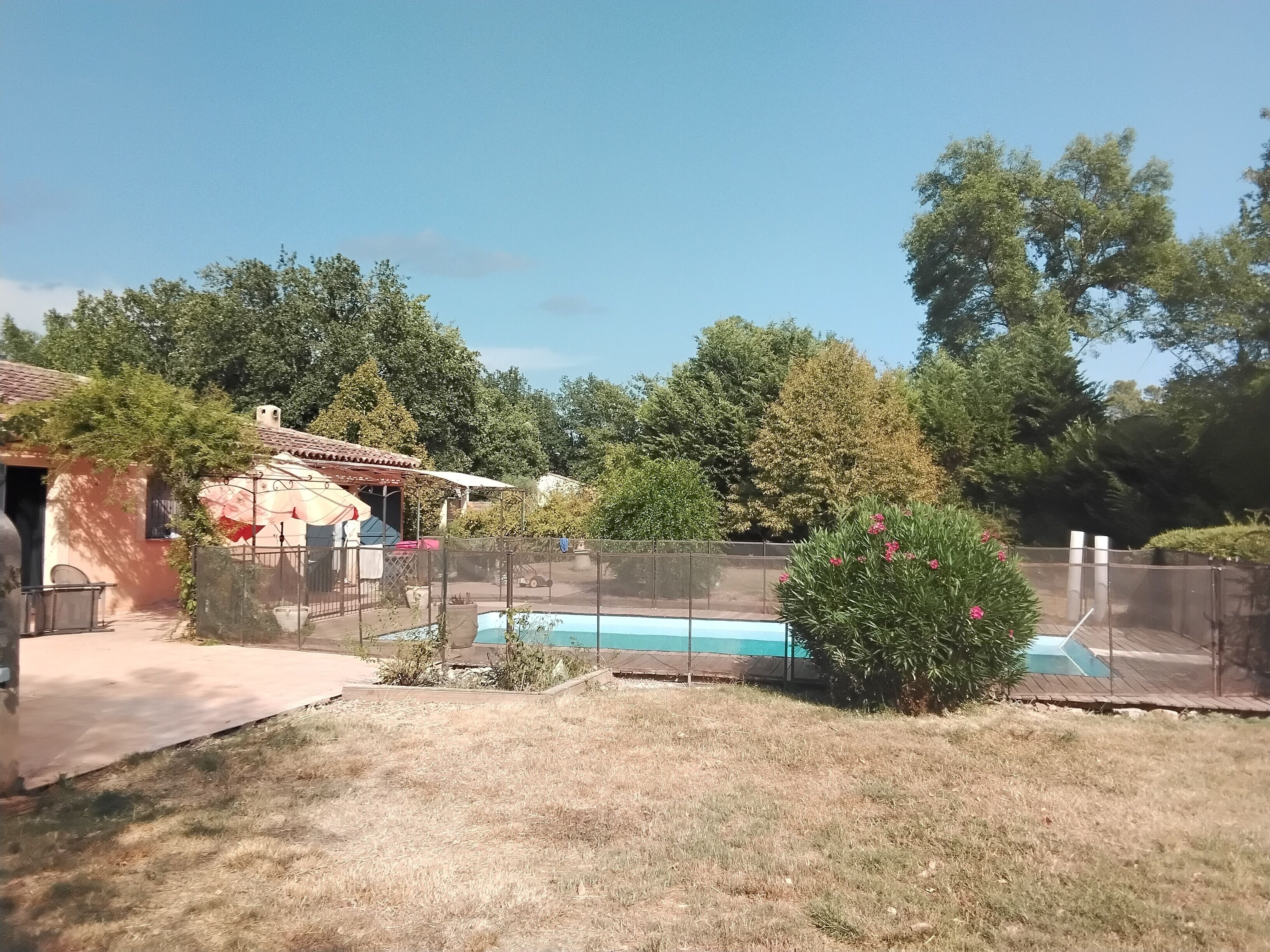 A backyard with a swimming pool, a fenced area, and a house with a tiled roof.