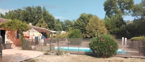 A backyard with a swimming pool, a fenced area, and a house with a tiled roof.