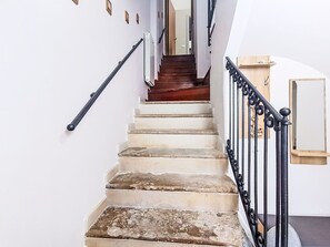 Una escala amb barana, terra de fusta i una paret blanca amb una porta a dalt.