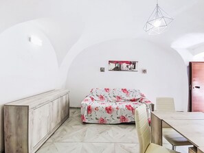 Habitació amb paret blanca, una banca de fusta, un sofà floral, una taula de dinar i una làmpada penjant.
