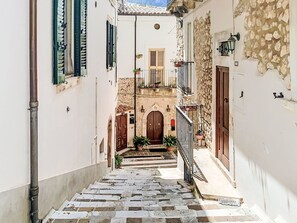 A narrow street with stone steps leading to a building with a wooden door and a balcony with potted plants. - Majella Living by Interhome (Caramanico Terme)