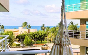 Ein Balkon mit Blick auf das Meer, Palmen und ein Gebäude mit blauer Fassade.