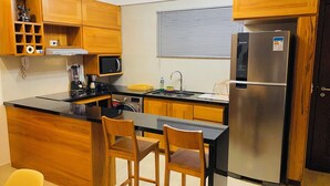A modern kitchen with wooden cabinets, a stainless steel refrigerator, a microwave, and a coffee maker. - Deluxe Apartment with Sea View & Pool Cumbuco (Praia de Cumbuco)