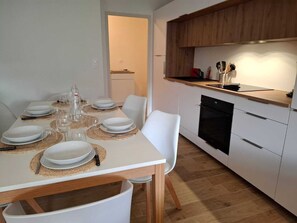 A modern kitchen with white cabinetry, a built-in oven, and a dining area with a table set for four. - 4-bedroom apartment (6 people), 70 m²—5-minute walk to the beach, 600 m from downtown, with a terrace and spa; quiet and cool (Binic-Étables-sur-Mer)