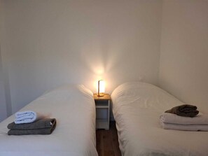 A single bed with a nightstand, a lamp, and folded towels. - 4-bedroom apartment (6 people), 70 m²—5-minute walk to the beach, 600 m from downtown, with a terrace and spa; quiet and cool (Binic-Étables-sur-Mer)