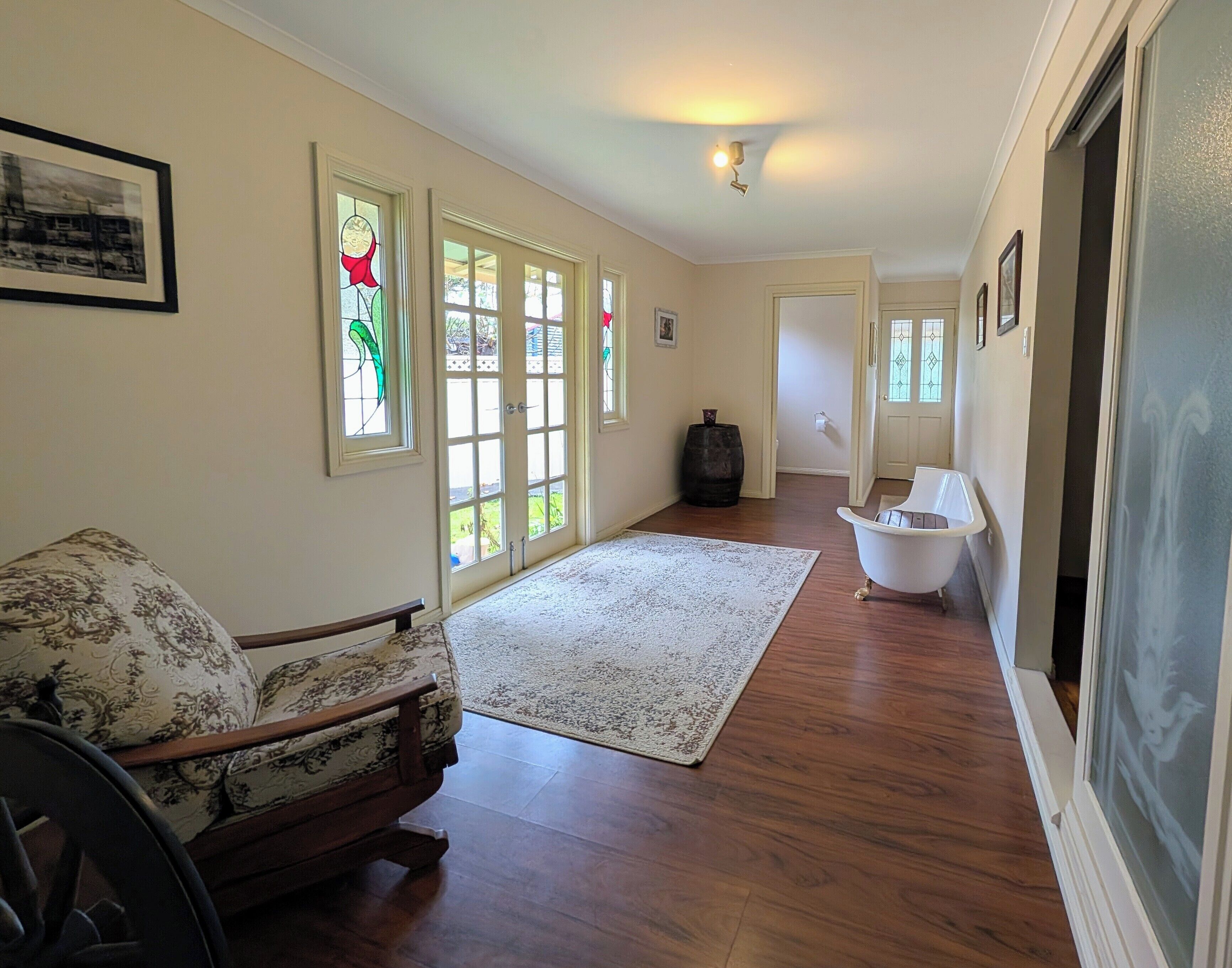 A spacious hallway with a wooden floor, a white bath tub, and a patterned sofa.