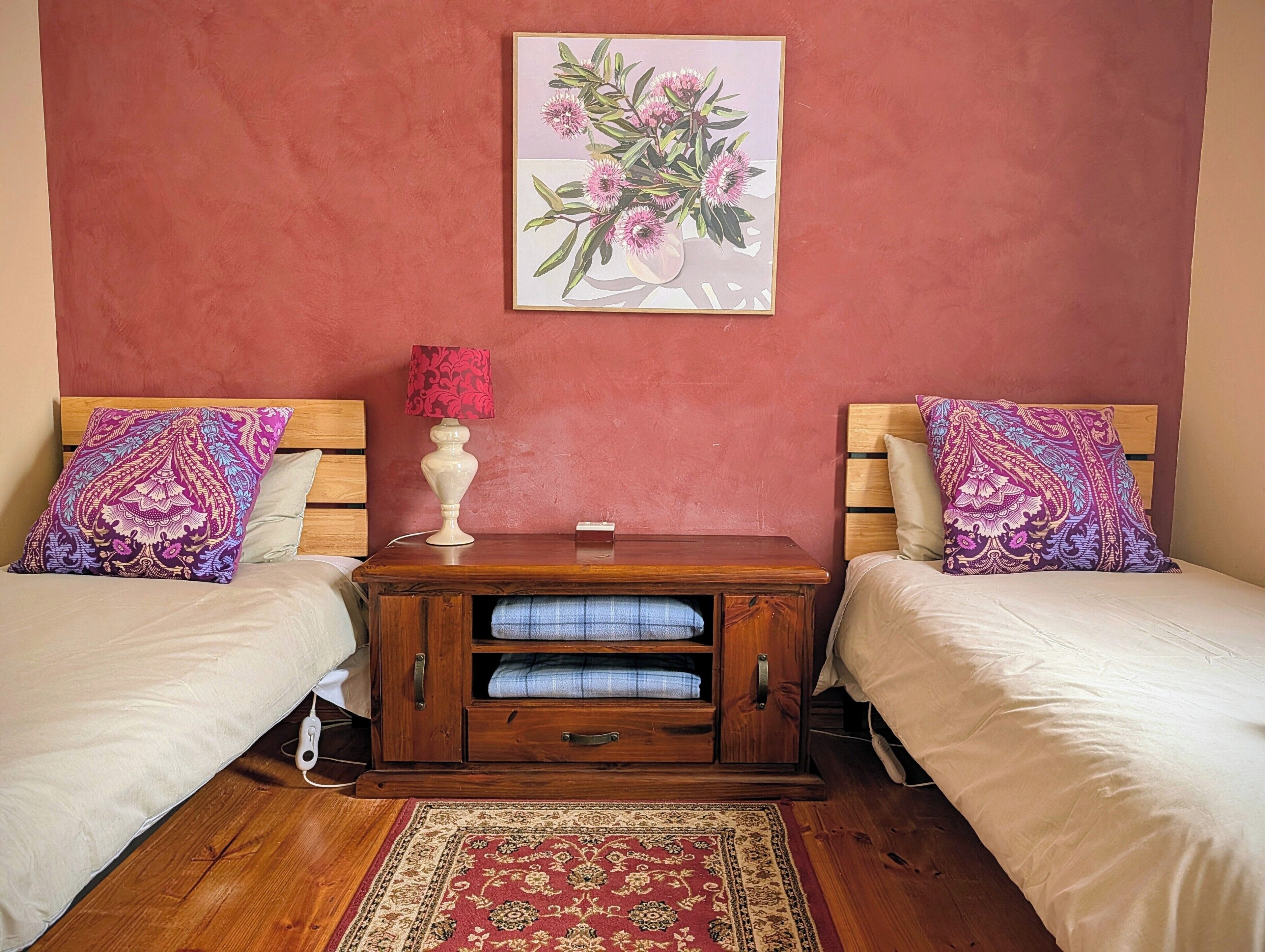 A bedroom with two beds, a nightstand, a lamp, and a floral artwork on the wall.