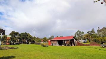 A grassy field with a picnic table, a red-roofed building, and a playground.