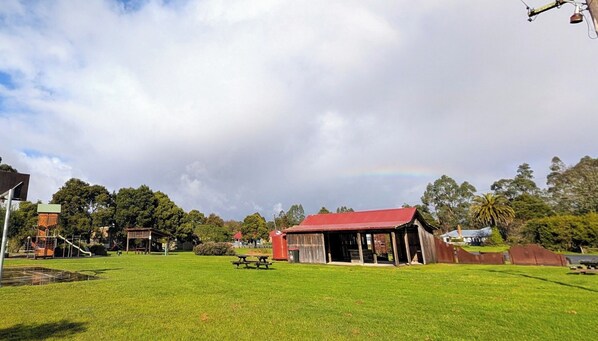 A grassy field with a picnic table, a red-roofed building, and a playground.