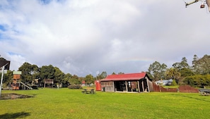 A grassy field with a picnic table, a red-roofed building, and a playground.