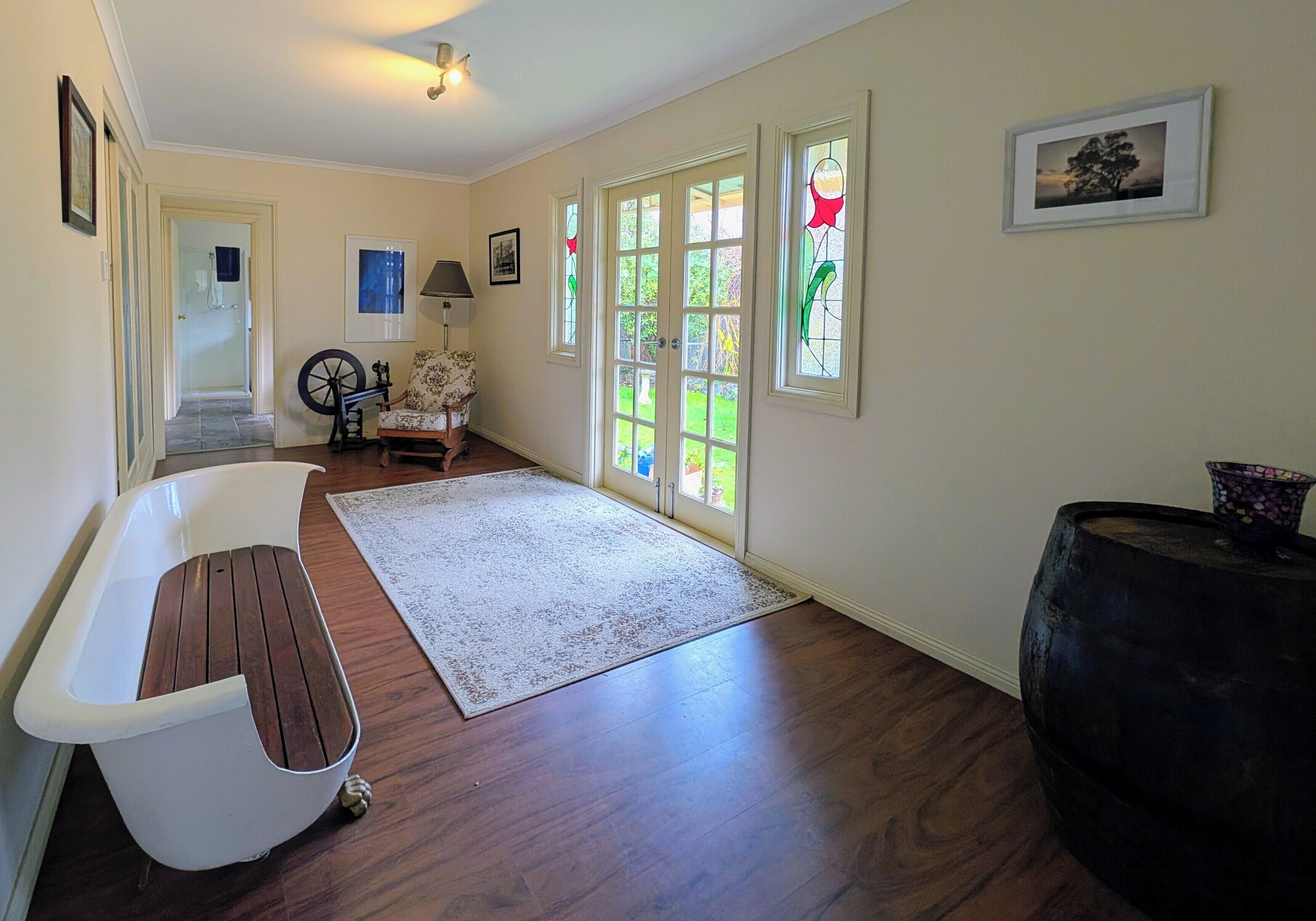A spacious room with hardwood flooring, a white bathtub, a large window with multiple panes, and a door leading to another room.