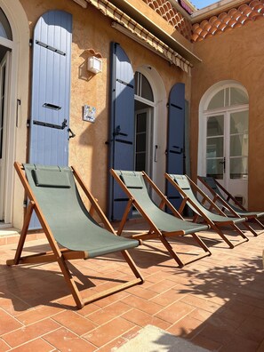 Eine Reihe von Liegestühlen vor einem Gebäude mit blauen Türen und einer gefliesten Terrasse.