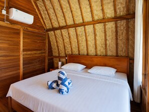Una habitación con techo de madera, una cama con ropa blanca y un equipo de aire acondicionado instalado en la pared.