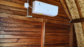 A room with wooden walls, a sloped ceiling, and a white air conditioning unit mounted on the wall. - Cozzy Bilva Garden (Klungkung)