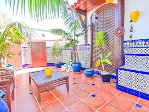 Un patio con suelo de baldosas, una mesa de madera, plantas en macetas y una pared decorativa.