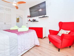 Et soveværelse med en seng, en rød lænestol, et fjernsyn og en hvid garderobe.