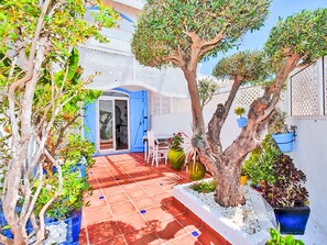 Eine Terrasse mit gefliestem Boden, einer blauen Tür und Topfpflanzen.