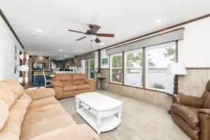 Un salon spacieux doté d’une grande fenêtre, d’un ventilateur de plafond et offrant une vue sur un lac.
