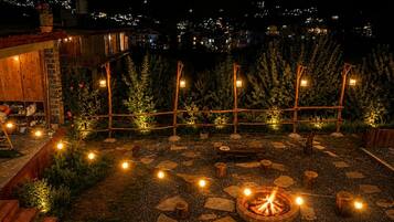 Un espace extérieur aménagé en terrasse, avec un foyer, des guirlandes lumineuses et une plateforme en bois.