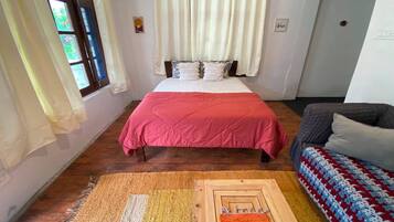 A bedroom with a bed, a sofa, and a patterned rug.