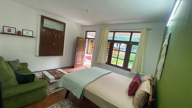 Een slaapkamer met een bed, een groene bank, een houten deur en een raam met uitzicht.