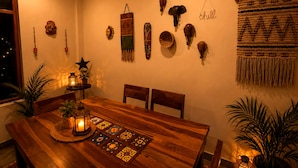Een eethoek met een houten tafel, stoelen, een decoratieve wand met diverse objecten en een macramé hangwerk.