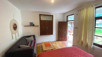 Ein Zimmer mit einem Bett, einem Sofa, einem Holztisch, einer Tür und einem Fenster mit Vorhängen.