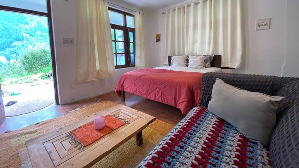 A bedroom with a bed, a sofa, a wooden coffee table, and a view of greenery outside. - Elevn Stays, Manali (Manali)