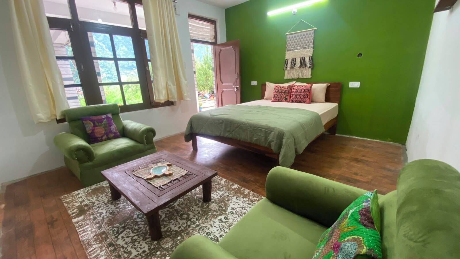 Une pièce comprenant un lit, deux canapés verts, une table basse en bois et un tapis à motifs.