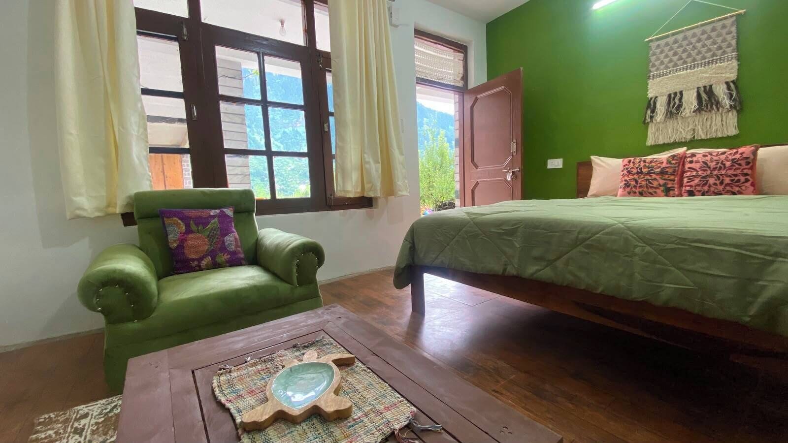 Une pièce avec un canapé vert, une table basse en bois ornée d’un objet décoratif, un lit recouvert d’une couverture verte et un mur vert agrémenté d’un textile suspendu.