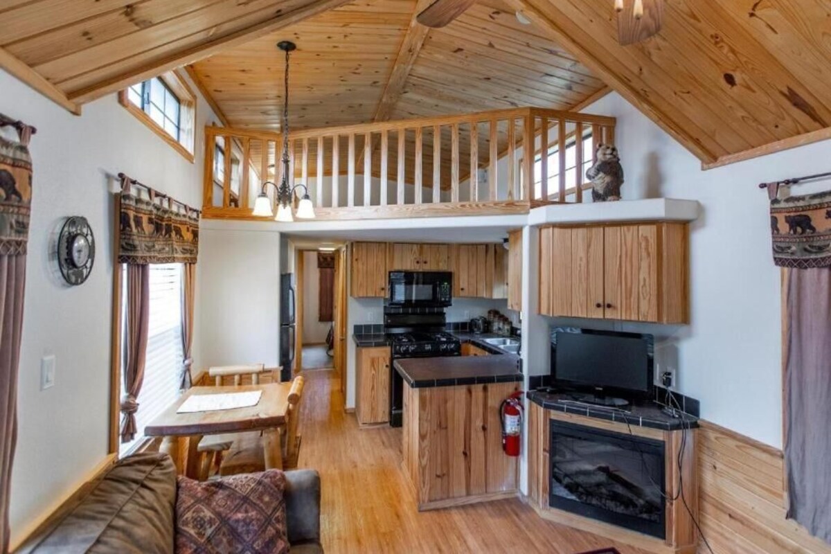 A cabin interior with a dining area, kitchen, and a loft bedroom.