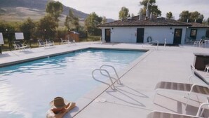 Una piscina con sillas de descanso y un edificio pequeño al fondo.