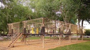 Estructura de juegos con zona de escalada en red, escalera de madera y plataforma con tobogán.