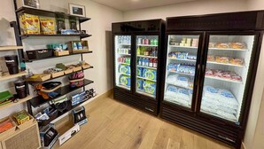 A room with shelves stocked with snacks and beverages, and two large refrigerators filled with various drinks and snacks.