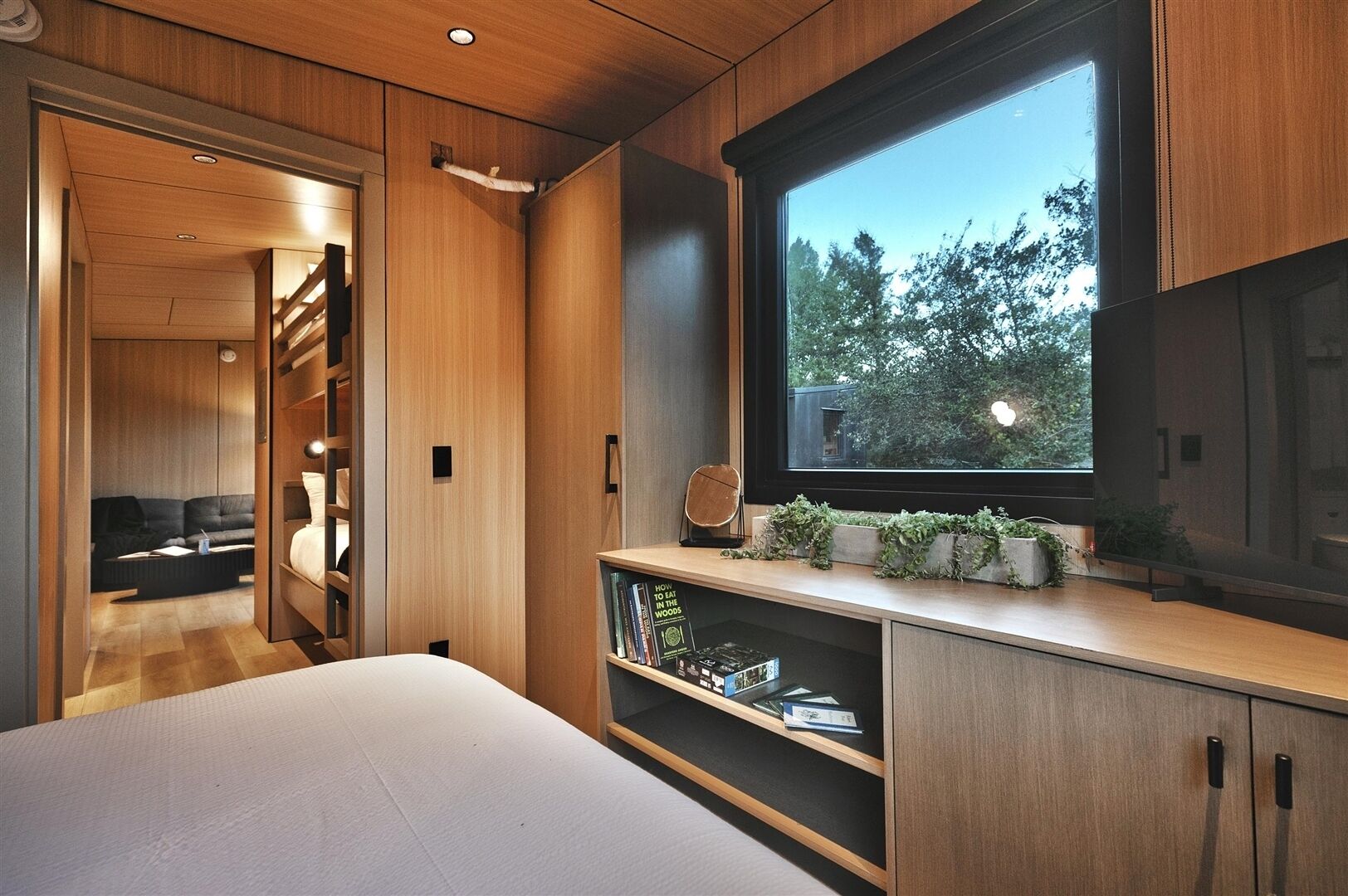 Un dormitorio moderno con un ventanal grande, estanterías empotradas y una zona de estar acogedora.