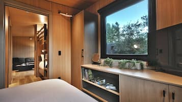Un dormitorio moderno con un ventanal grande, estanterías empotradas y una zona de estar acogedora.