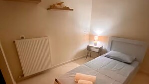 Une chambre à coucher comprenant un lit, une table de chevet avec une lampe, un radiateur et une étagère ornée d’objets décoratifs.