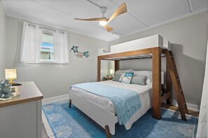 A bedroom with a bunk bed, a desk with a lamp, a ceiling fan, and a window with curtains. - 2BR Steps to Beach & Pool | Good Morning Rentals (Jacksonville Beach)