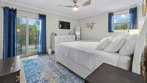Un dormitorio con cama, televisión, ventilador de techo y vista a palmeras a través de la ventana.