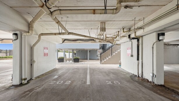 Un aparcamiento subterráneo con pilares de hormigón, tuberías y una escalera que conduce a un nivel superior.