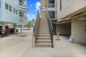 A multi-story building with a central staircase, a parking area with vehicles, and a sign indicating a rental property. - 2BR Steps to Beach & Pool | Good Morning Rentals (Jacksonville Beach)